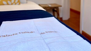 Een bed met een wit- en blauwe dekbedovertrek, een geel kussen met een bladpatroon en een hanglamp.