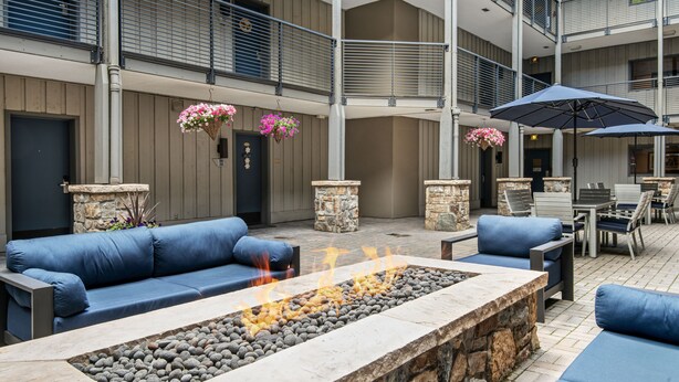 A spacious outdoor seating area with a stone fire feature, blue sofas, and hanging flower baskets.
