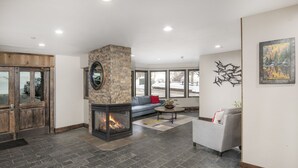 A modern living room with a stone fireplace, a grey sofa, and a large window offering a view of the outdoors.