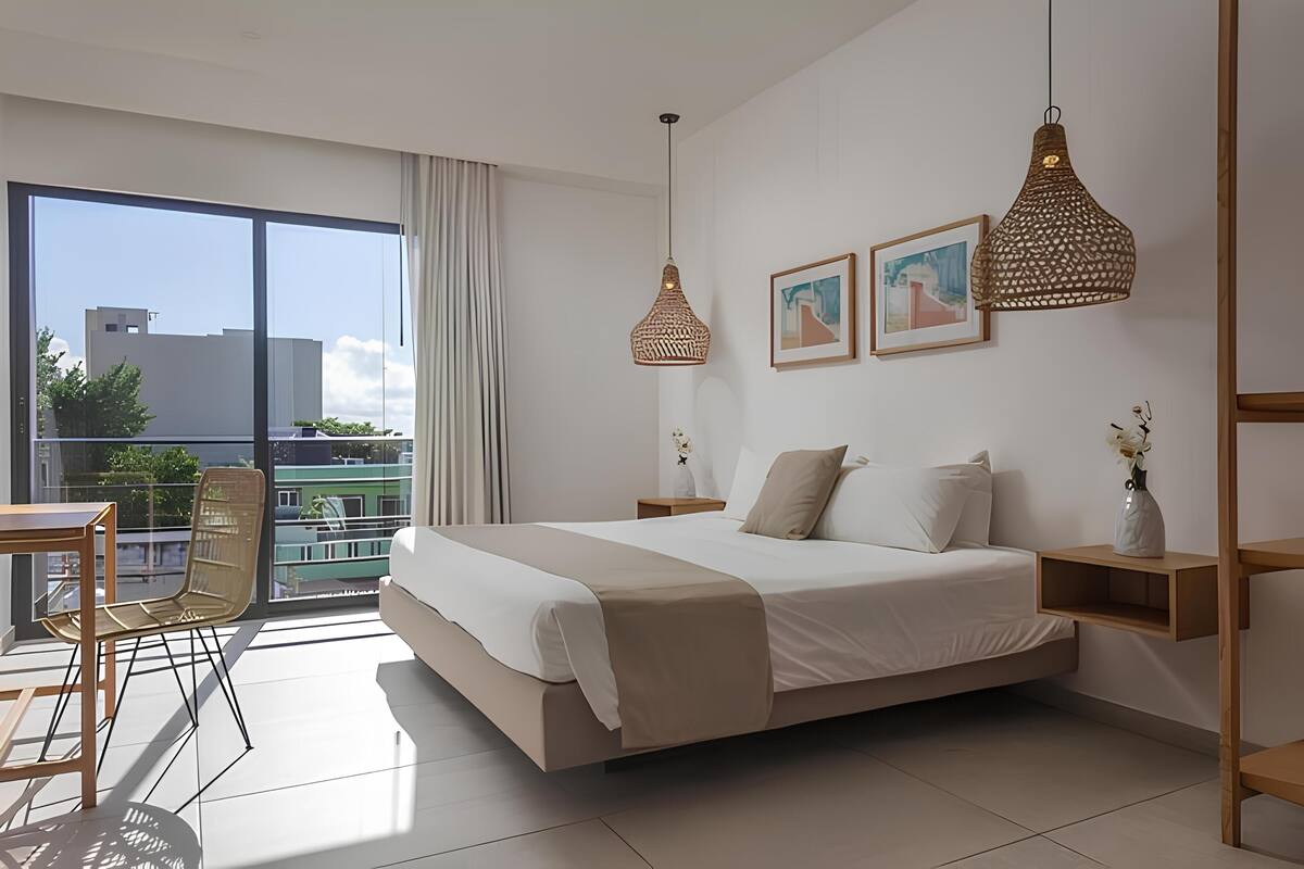 A modern bedroom with a large bed, two pendant lights, a nightstand, a small table, and a chair.