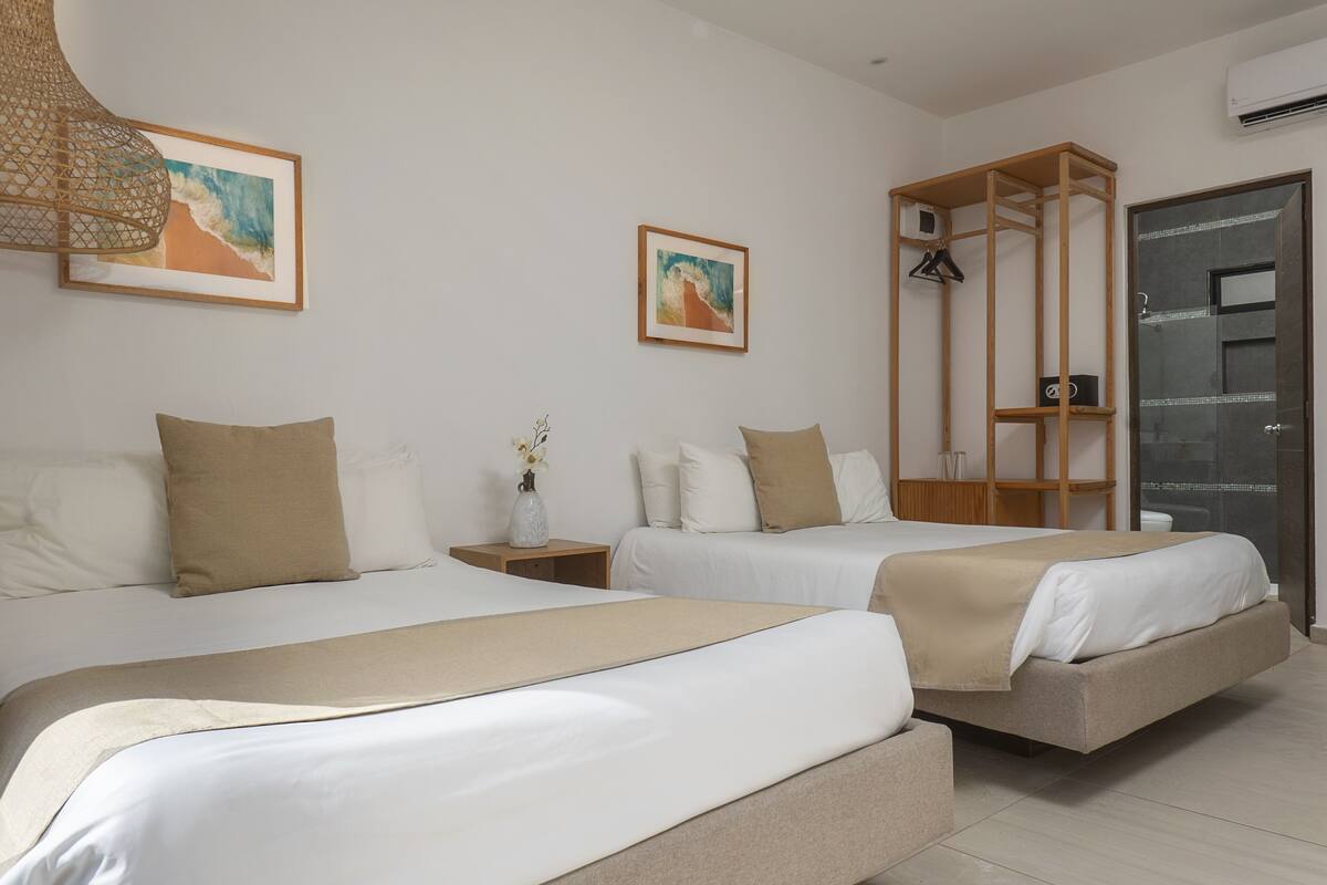 A modern hotel room with two beds, a wooden shelf unit, and artwork on the walls.