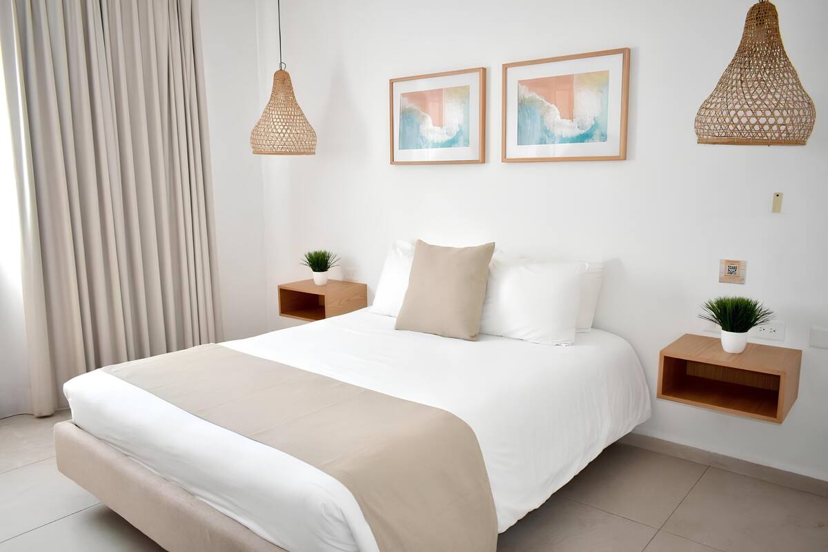 A modern bedroom with a large bed, two bedside tables with plants, and two wall-mounted light fixtures.