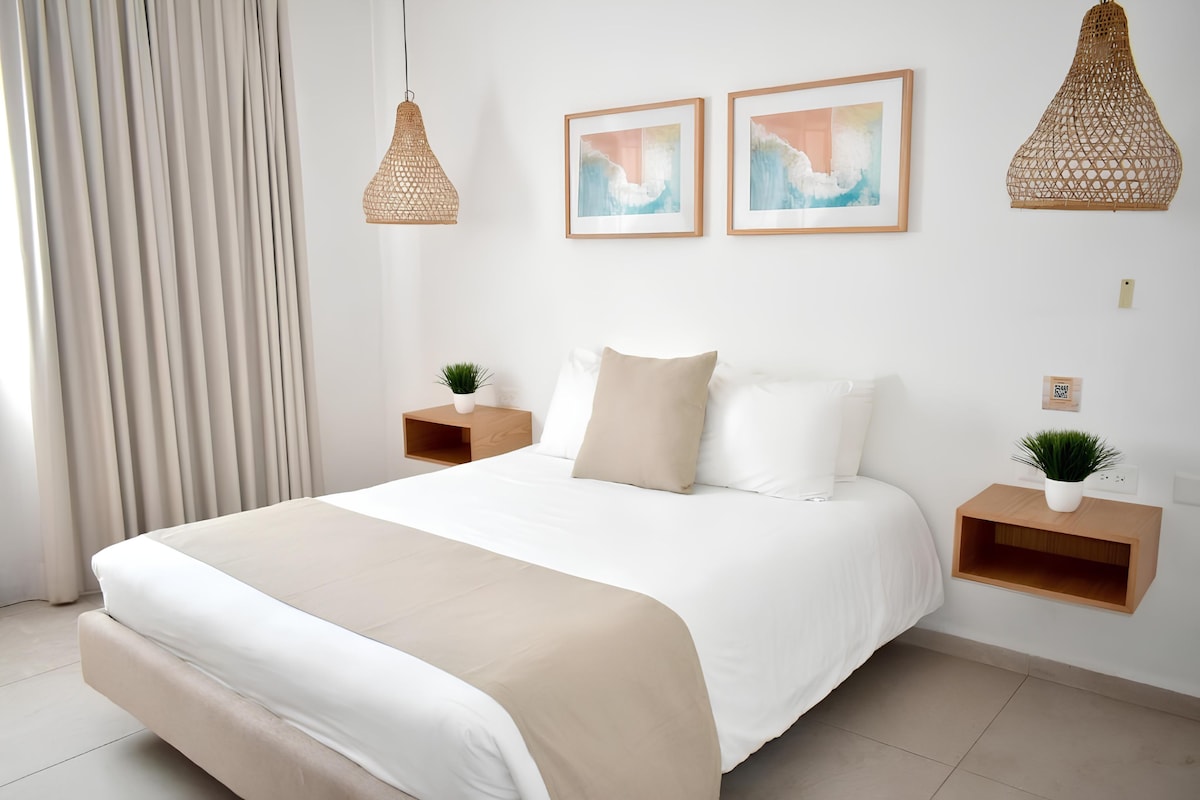 Un dormitorio moderno con una cama grande, dos mesitas de noche con plantas y dos lámparas de pared.