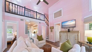Un salon spacieux avec un plafond haut, un escalier et un téléviseur fixé au-dessus d’un meuble en bois.