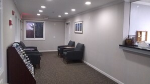 Una habitación con piso alfombrado, una ventana, un cuadro enmarco y un mostrador de recepción con espejo.