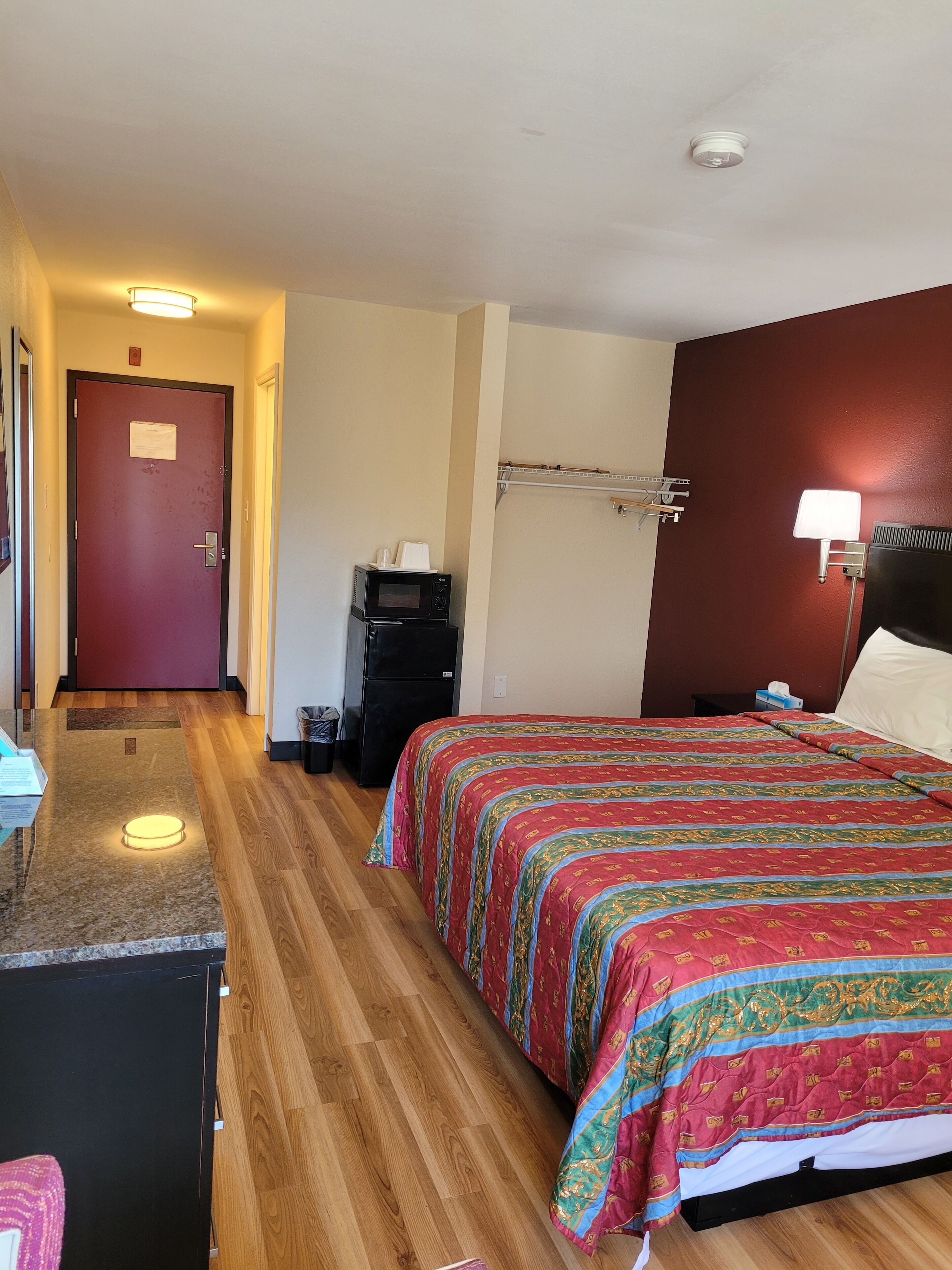 A hotel room with a bed, a desk, a microwave, and a refrigerator.