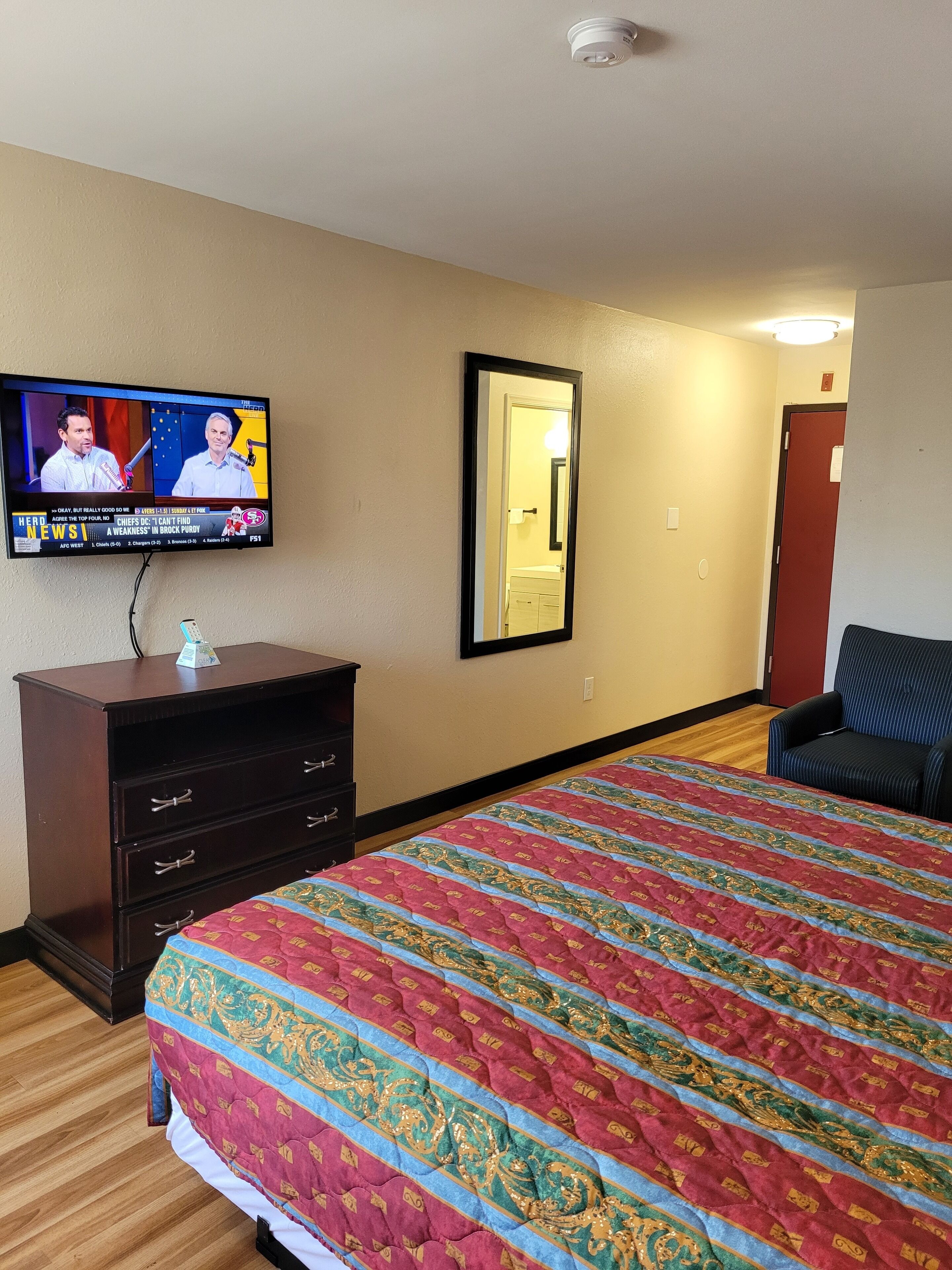 Ett hotellrum med en stor säng, en byrå, en tv och en spegel.