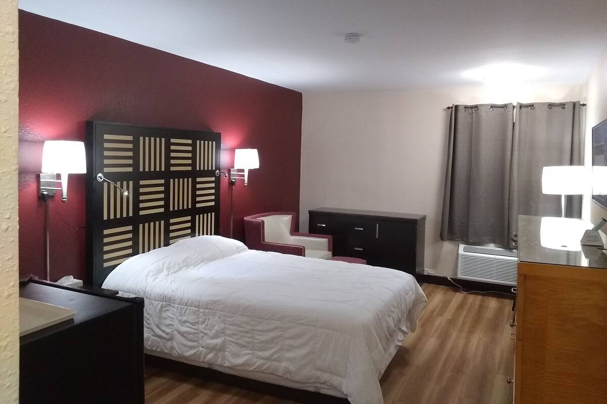 A hotel room with a bed, a desk, a chair, a wardrobe, and two wall-mounted lamps.