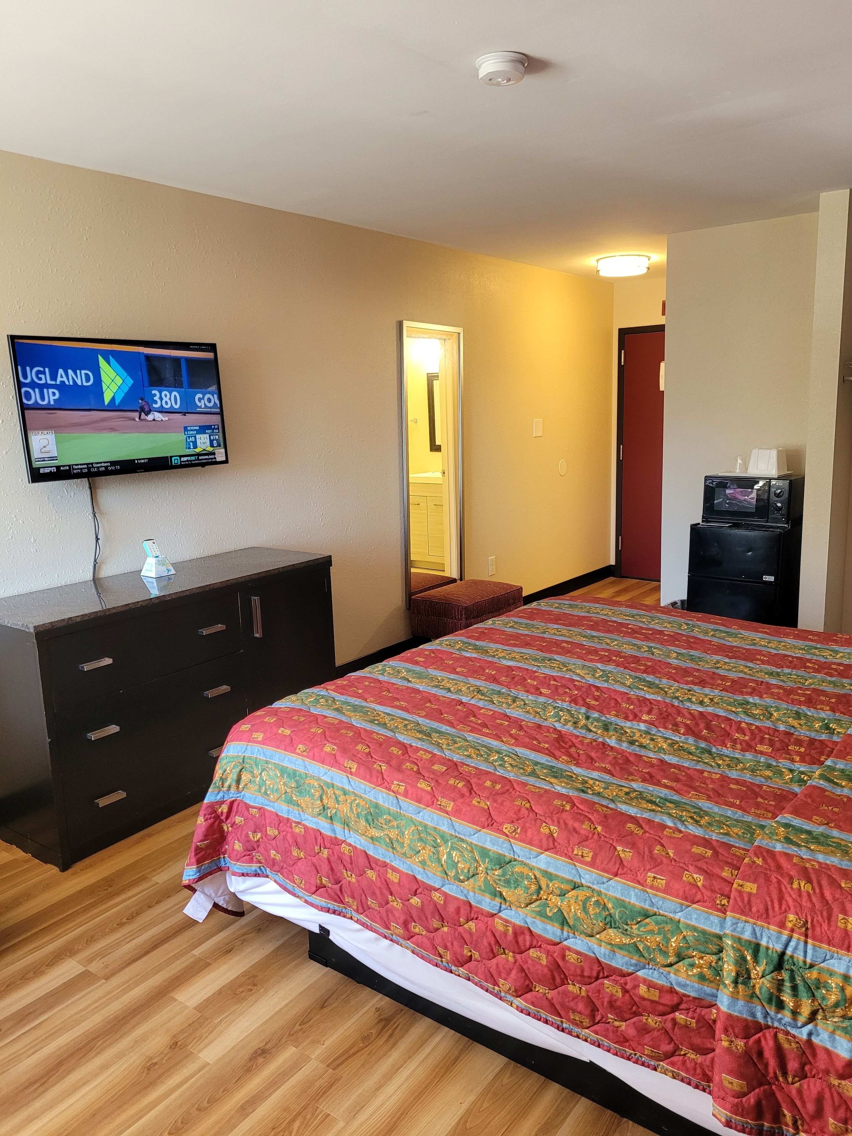 A hotel room with a large bed, a TV mounted on the wall, a dresser, and a microwave on the counter.