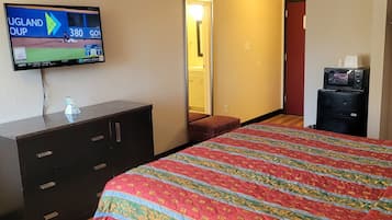 A hotel room with a large bed, a TV mounted on the wall, a dresser, and a microwave on the counter.