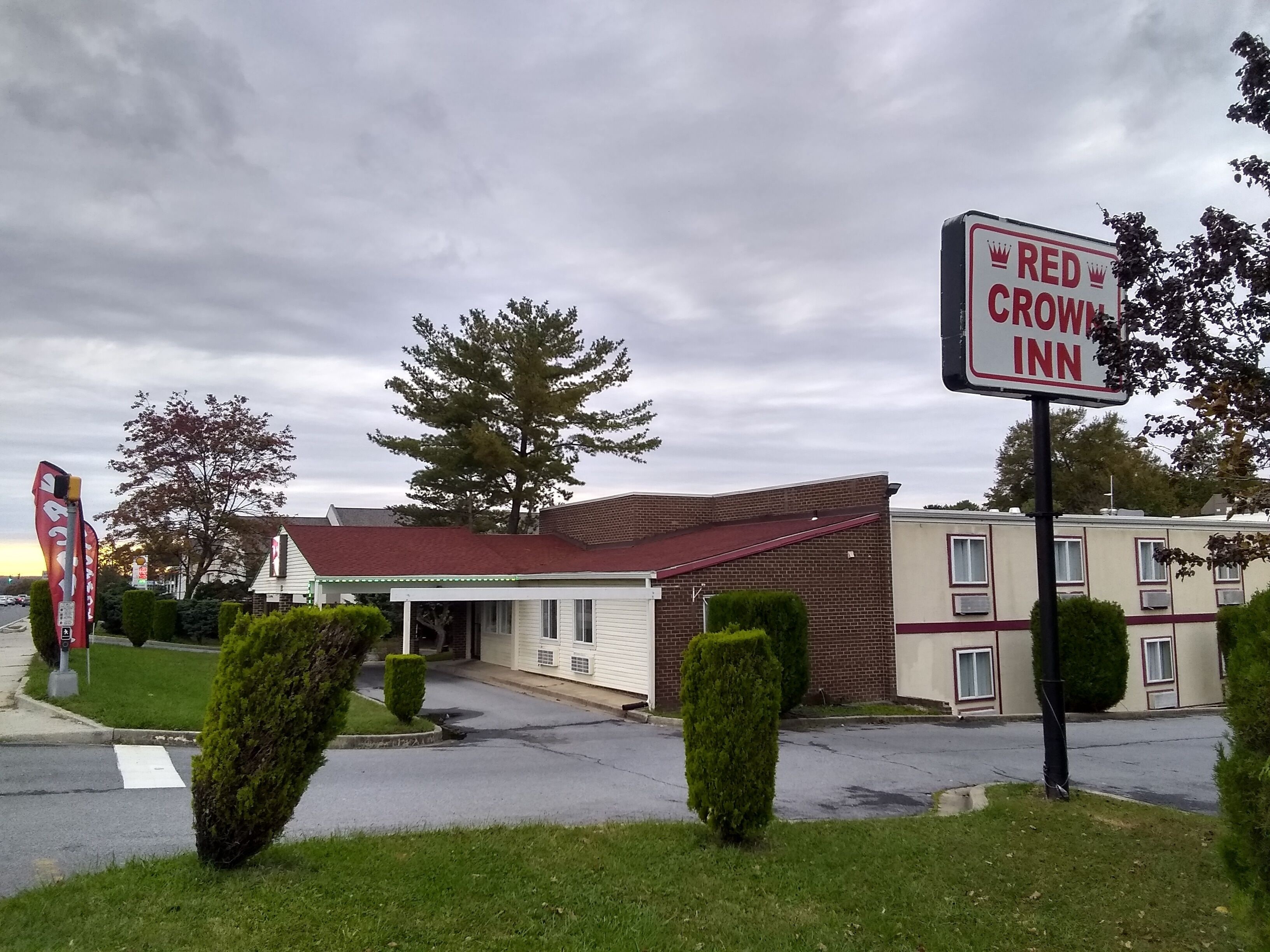 A Red Crown Inn with a brick facade and a red roof, surrounded by well-maintained lawns and a large tree.