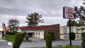 A Red Crown Inn with a brick facade and a red roof, surrounded by well-maintained lawns and a large tree.