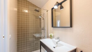 Une salle de bain avec une douche à parois de verre, un lavabo blanc et un miroir au-dessus du lavabo.