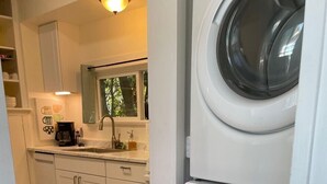 Une cuisine compacte dotée d’un lave-linge et d’un sèche-linge intégrés, d’un plancher en bois et d’une fenêtre donnant sur les arbres.