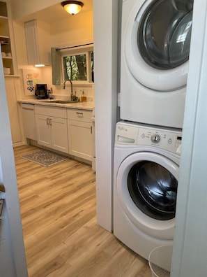 A compact kitchen with a built-in washer and dryer, wooden flooring, and a window with a view of trees.