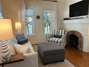 A living room with a sofa, ottoman, armchair, fireplace, and a television.