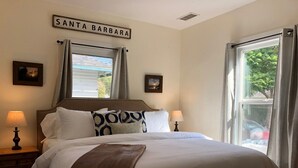 Un lit bien fait, recouvert d’un plaid marron, avec deux lampes de chevet et une pancarte au-dessus du lit sur laquelle on peut lire « SANTA BARBARA ».