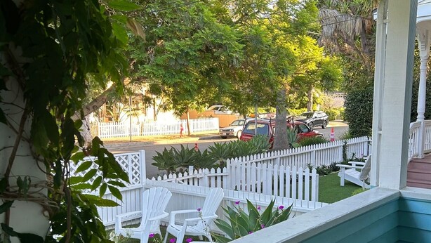 A covered porch with a white picket fence, outdoor seating, and a view of the street.