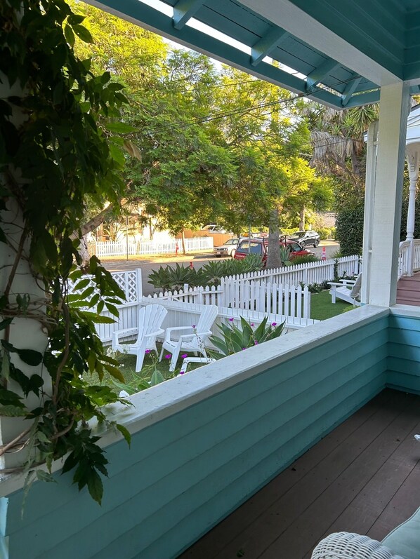 A covered porch with a white picket fence, outdoor seating, and a view of the street.