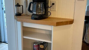 Une cuisine équipée d’une machine à café, d’un moulin à café et de capsules de café rangées sur une étagère.
