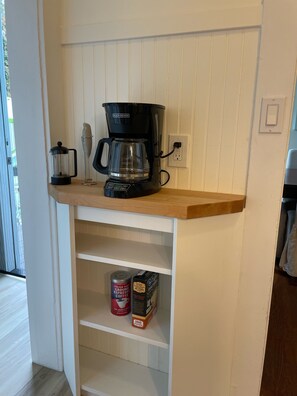A kitchen with a coffee maker, a coffee grinder, and coffee pods on the shelf.