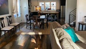 A spacious living area with a wooden floor, a large sofa, and a dining table.