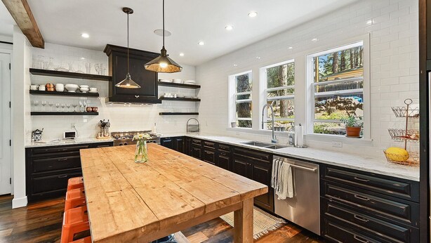 A modern kitchen with a wooden table, black cabinets, and a large window.