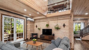 A cozy log cabin interior with a fireplace, a TV, and a balcony. - New Luxury Cabin w/ King Beds, Game Room and Fire Pit  (Eureka Springs)