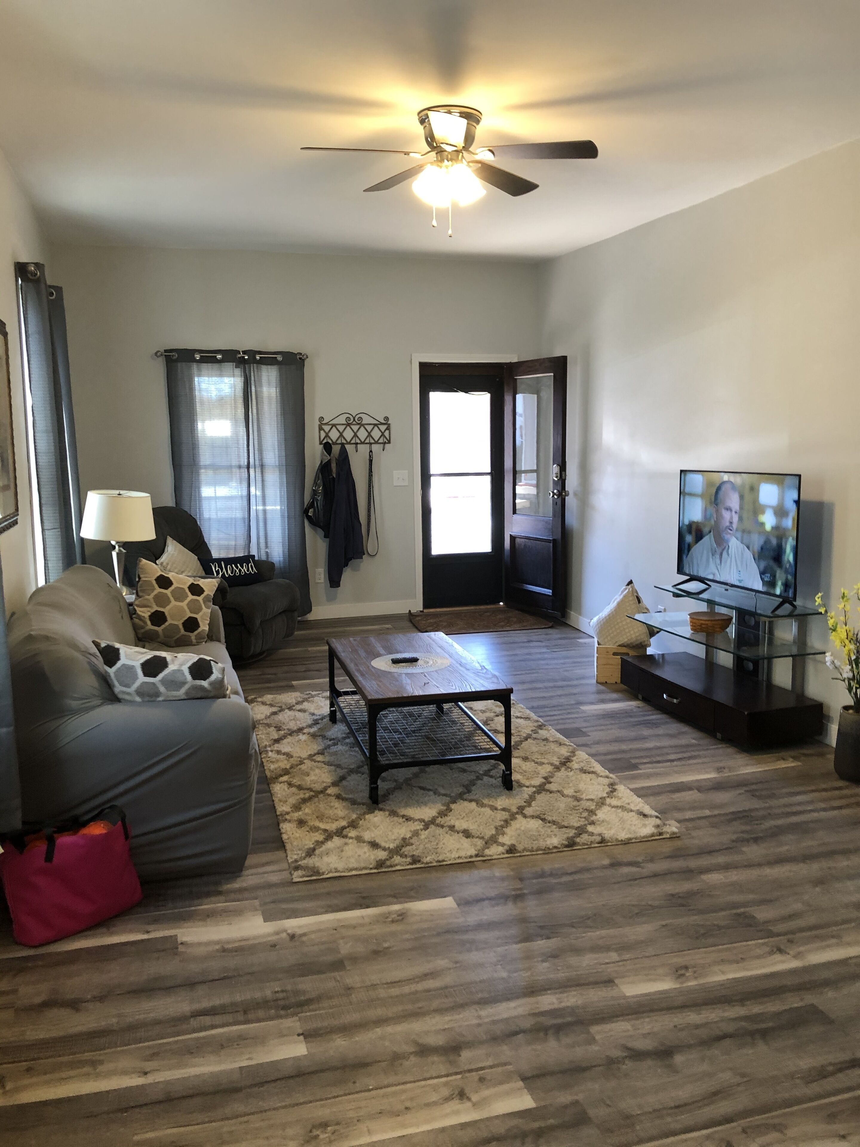 A living room with a ceiling fan, a TV, a sofa, a coffee table, and a door leading to another room.