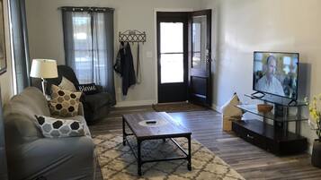 A living room with a ceiling fan, a TV, a sofa, a coffee table, and a door leading to another room.