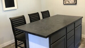 A modern kitchen with a central island, black chairs, white cabinets, and a framed picture on the wall.