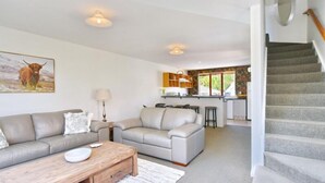 A living room with a sofa and a coffee table, a kitchen with a bar area, and a staircase. - Central Akaroa Retreat - Balcony & Parking -Tumeke Akaroa (Akaroa)