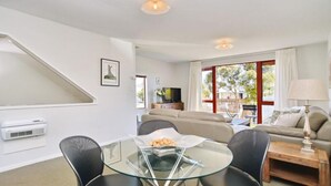 A modern living room with a glass coffee table, a sofa, and a TV. - Central Akaroa Retreat - Balcony & Parking -Tumeke Akaroa (Akaroa)