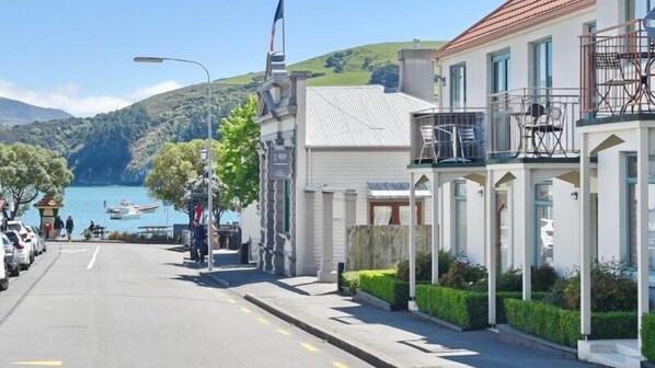 A coastal street with a row of buildings, a clear view of the sea, and parked cars along the road.