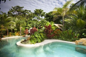 A pool surrounded by lush tropical vegetation and a clear sky. - Azania Bungalows (Puerto Viejo de Talamanca)