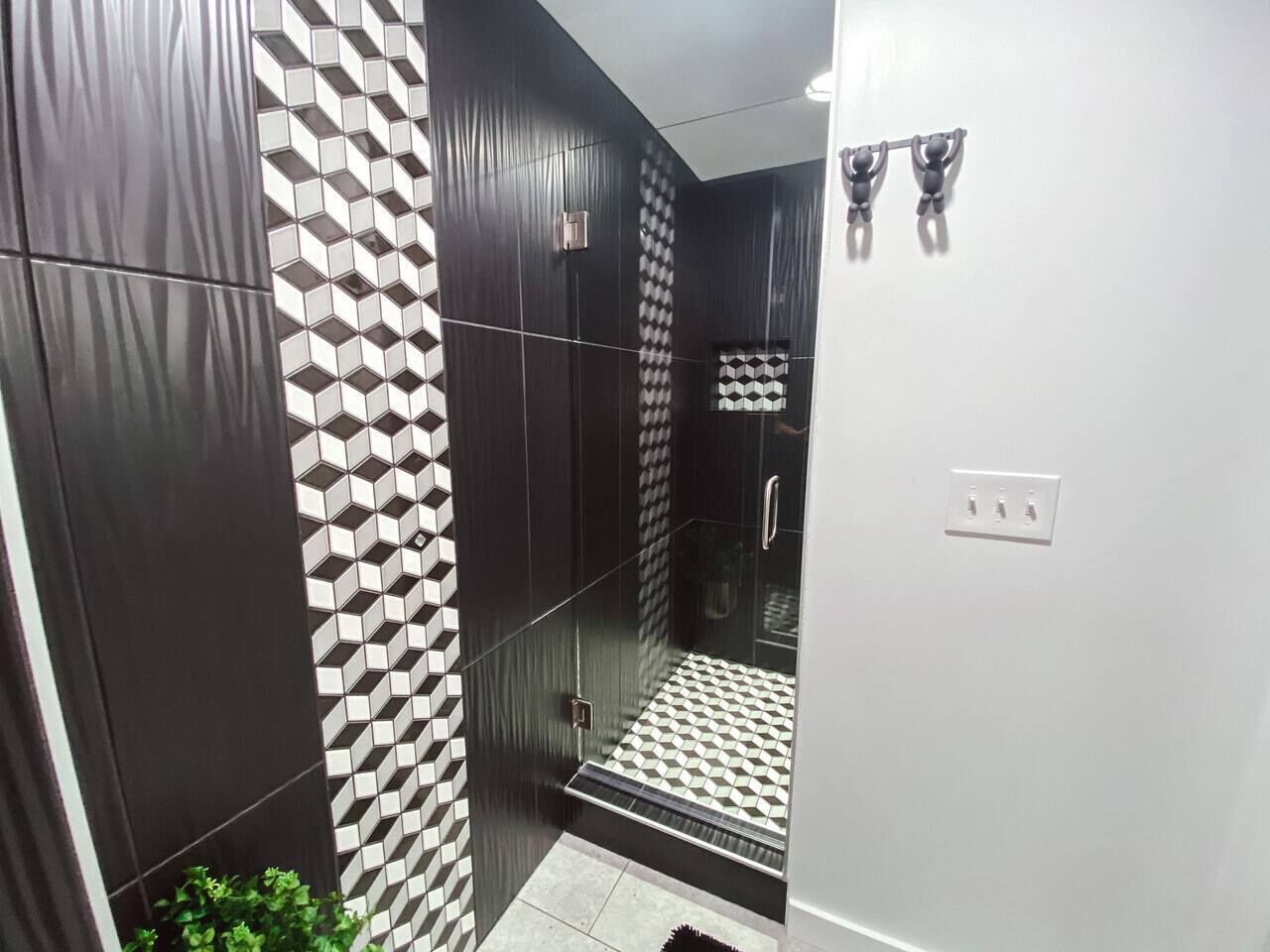 Un baño moderno con pared de azulejos blanco y negro, cabina de ducha de cristal y zona de lavabo blanca.