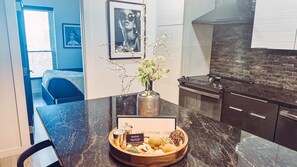 A modern kitchen with dark countertops, a stainless steel range hood, and a brick backsplash. A wooden bowl with various pastries and a sign reading "Heir-Livin" is on the counter.