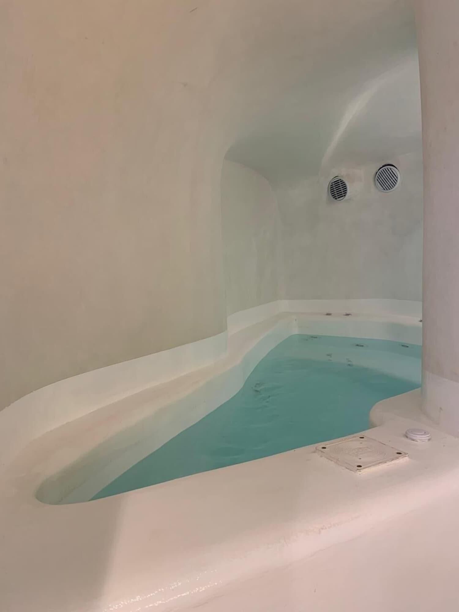 A bathtub with a light blue interior, white walls, and two small vents on the ceiling.