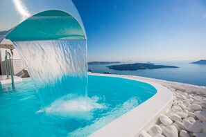 Una piscina con fuente de agua, rodeada de piedras blancas y vistas a un paisaje costero.