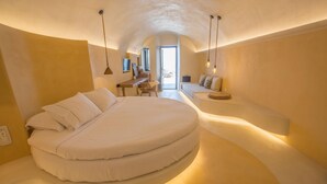 A circular bed in a room with a curved ceiling, a desk, and a seating area with cushions. - Chic Hotel Santorini (Santorini)