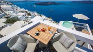 A terrace with a wooden table, two wicker chairs, and a view of the sea with boats. - Chic Hotel Santorini (Santorini)