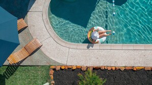 Una piscina con cubierta de baldosas, un banco de madera y un borde de piedra.