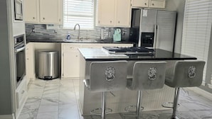Una cocina moderna con armarios blancos, encimera negra, refrigerador de acero inoxidable y pileta doble.