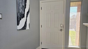 Un pasillo con una puerta blanca, un felpudo negro y un cuadro abstracto grande en la pared.