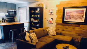 Ein modernes Wohnzimmer mit einem Ecksofa, einem Couchtisch und einer Küchenzeile inklusive Mikrowelle.