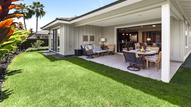 A modern house with a covered patio, a lawn, and a dining area with outdoor furniture.