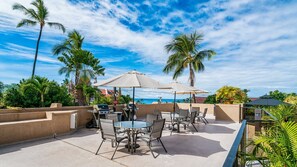 Enjoy al fresco dining with ocean views from this patio area, featuring barbecue grills and tables under shaded umbrellas.