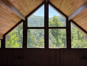 Une pièce dotée d’un plafond en bois incliné et d’une grande fenêtre offrant une vue sur une montagne boisée.