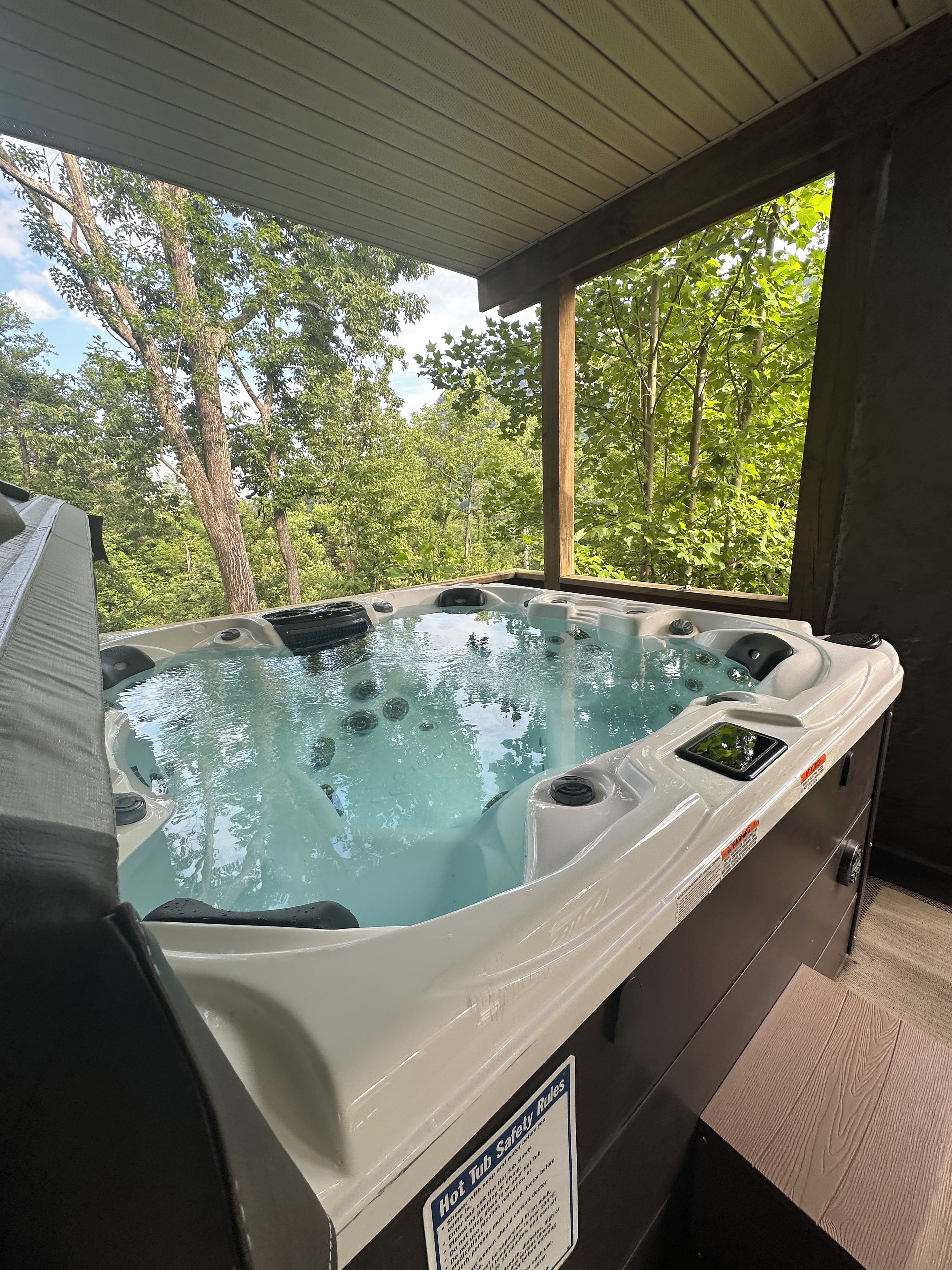 Un bain à remous doté d’un panneau de sécurité, entouré d’arbres et bordé d’une terrasse en bois.
