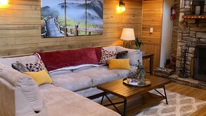 Ein gemütliches Wohnzimmer mit Holzbalkendecke, einem Steinkamin und einem großen Gemälde einer Waldszene.